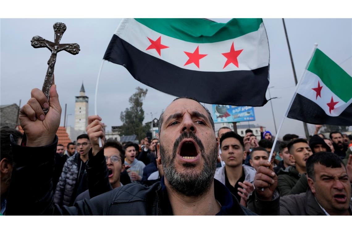 Bilder des Tages Ein syrischer Christ hält ein Kreuz hoch und ruft Parolen bei einem Protestmarsch in Damaskus, nachdem am Montagabend Unbekannte in Al-Sukailabija in der syrischen Provinz Hama den Weihnachtsbaum in Brand gesetzt hatten.