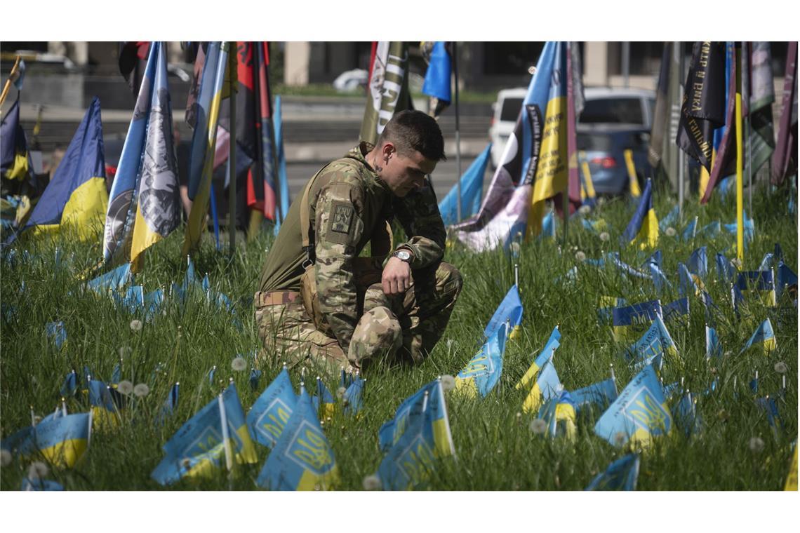 Wie ist Frieden in der Ukraine möglich? Ein ukrainischer Soldat legt auf dem Unabhängigkeitsplatz in Kiew eine kleine Nationalfahne auf den Rasen, um an einen Kameraden zu erinnern, der bei einem Gefecht mit russischen Truppen gefallen ist.
