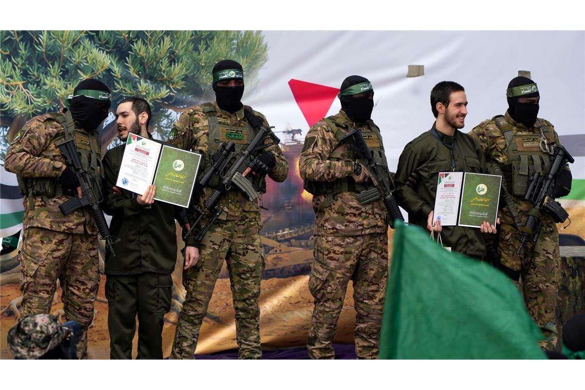 Angehörige berichten von Misshandlungen der Gaza-Geiseln Ein vermummter Hamas-Kämpfer gibt einer israelischen Geisel Anweisungen während einer Übergabe-Veranstaltung im Gazastreifen.