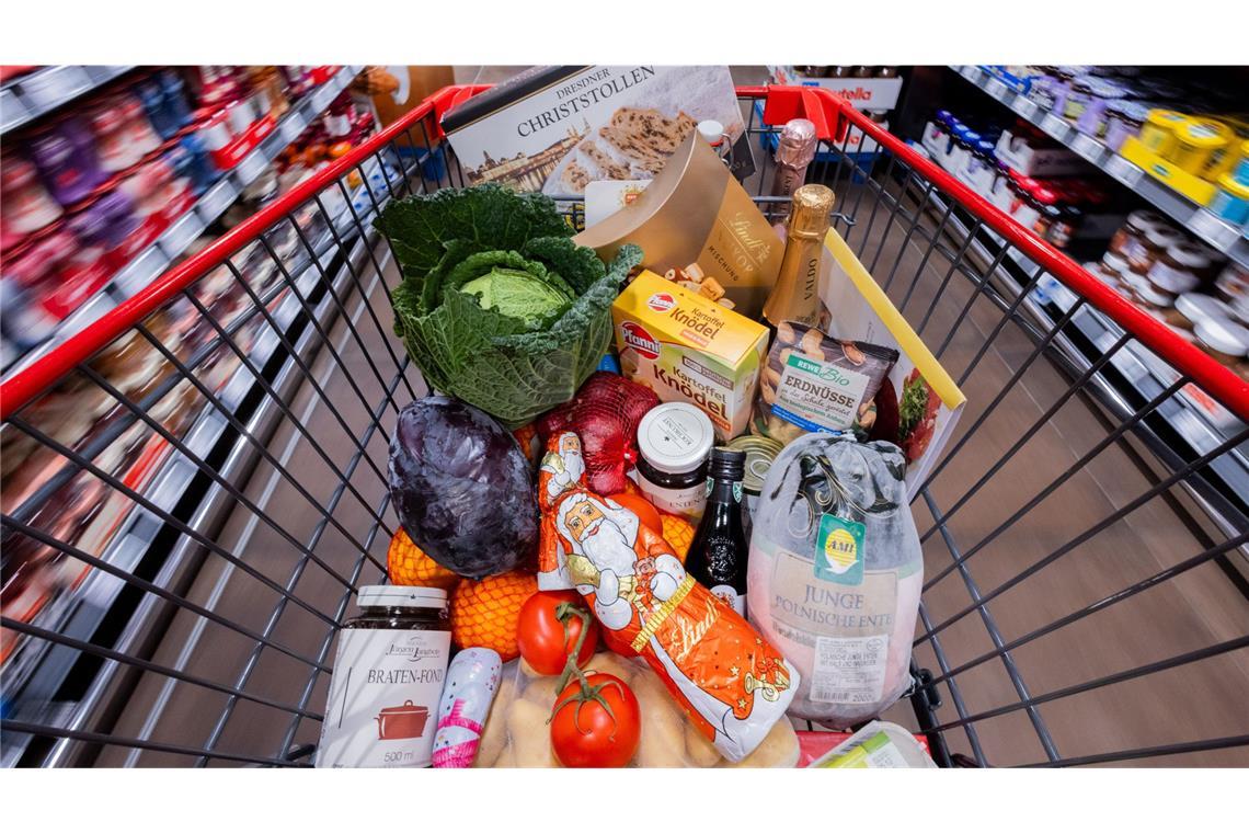 Alles wird teurer - auch Weihnachten Ein voller Einkaufswagen mit einer Polnischen Ente, Gemüse, Obst, Christstollen, Knödel, Sekt, Wein, Pralinen und Schokoladen-Weihnachtsmännern wird an Regalen vorbei in einem Supermarkt geschoben