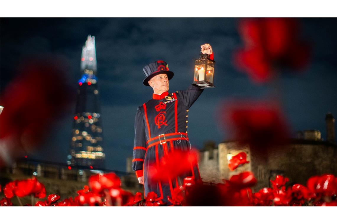 Ein Yeoman Warder (Beefeater) des Tower of London hält eine Laterne bei einer Ausstellung von Keramik-Mohnblumen im Tower anlässlich des Armistice Day.