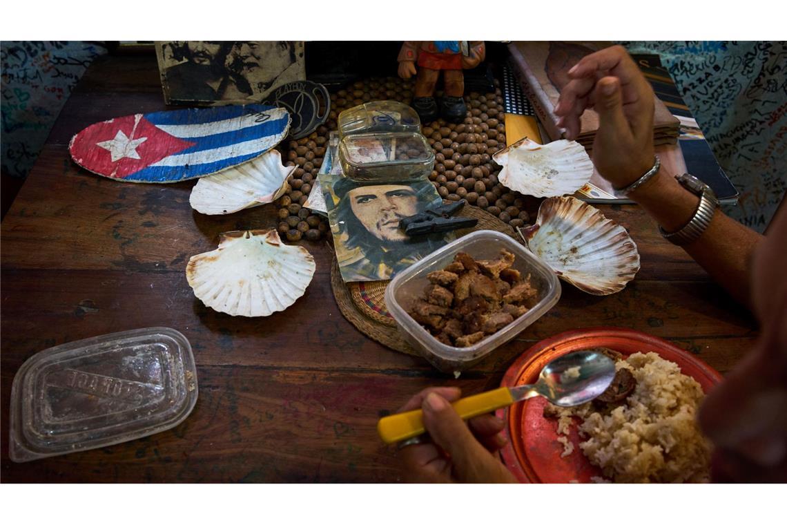 Eine Angestellte eines Souvenirgeschäfts in Havanna isst neben Bildern von Che Guevara, Fidel Castro und Ernest Hemingway.