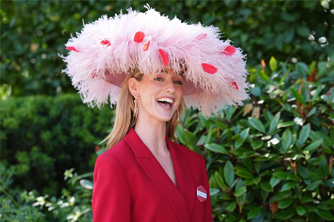 Eine Besucherin von Royal Ascot kombiniert einen roten Hosenanzug mit einem großen, hellrosa Federhut. Rote Blütenblätter setzen farbliche Akzente und greifen den Ton des Outfits wieder auf.