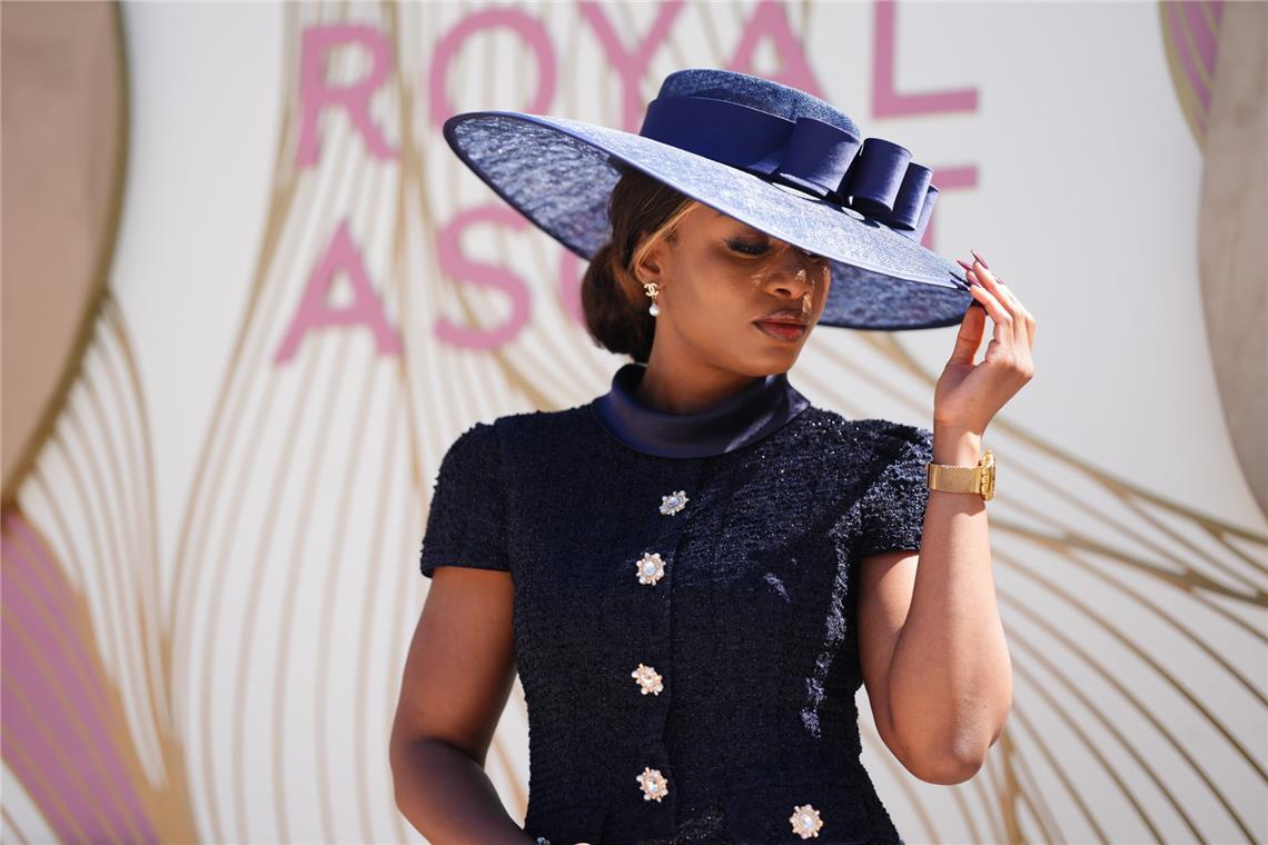 Eine Besucherin von Royal Ascot zeigt einen besonders eleganten Ton-in-Ton-Look in Dunkelblau: Der breitkrempige Hut mit Schleifendetail passt zum strukturierten Kleid mit Schmuckknöpfen und wirkt klassisch, zurückhaltend und sehr edel.