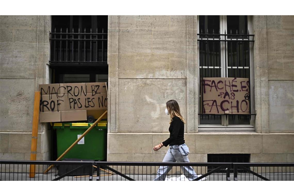 Eine Demonstrantin geht an Plakaten vorbei, auf denen steht „Macron, fick deine Lehrerin, nicht unsere“ (l) und „Wütend, keine Faschisten“ (r), während der Blockade eines Gebäudes der Sciences Politiques im Rahmen der landesweiten Proteste.