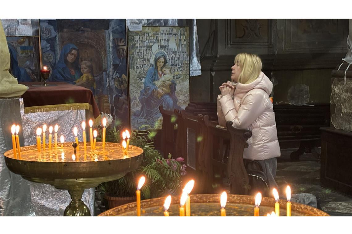 Kaffee, Tee und Wut auf Trump Eine Frau betet in der Garnisonskriche von Lwiw um Frieden. Zu ihrer Rechten sind Gemälde aufgestellt, die die Gottesmutter Maria inmitten der Trümmern durch russische Bomben zerstörte Wohnhäuser aber auch auf dem Schlachtfeld zeigen.