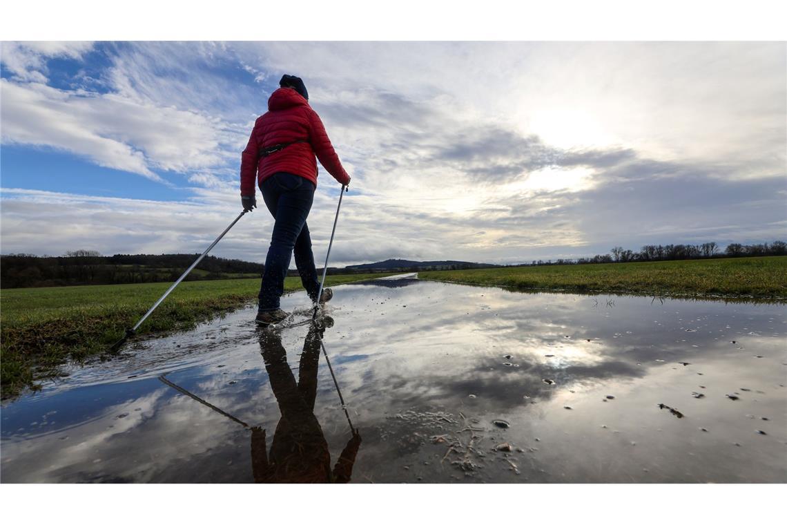 Bilder des Tages Eine Frau geht am vierten Advent mit Nordic Walking Stöcken durch eine Regenpfütze, in der sich der Himmel widerspiegelt.
