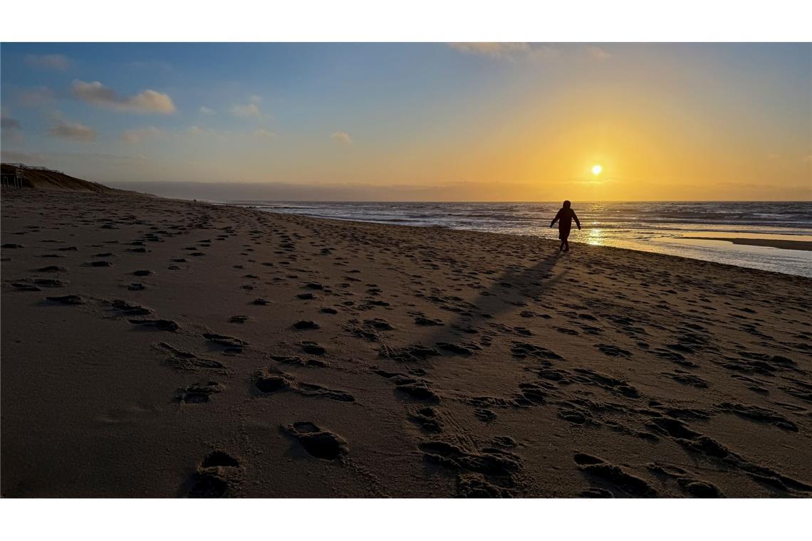 Eine Frau geht im Licht der tief stehenden Sonne am Strand bei Rantum auf Sylt spazieren.