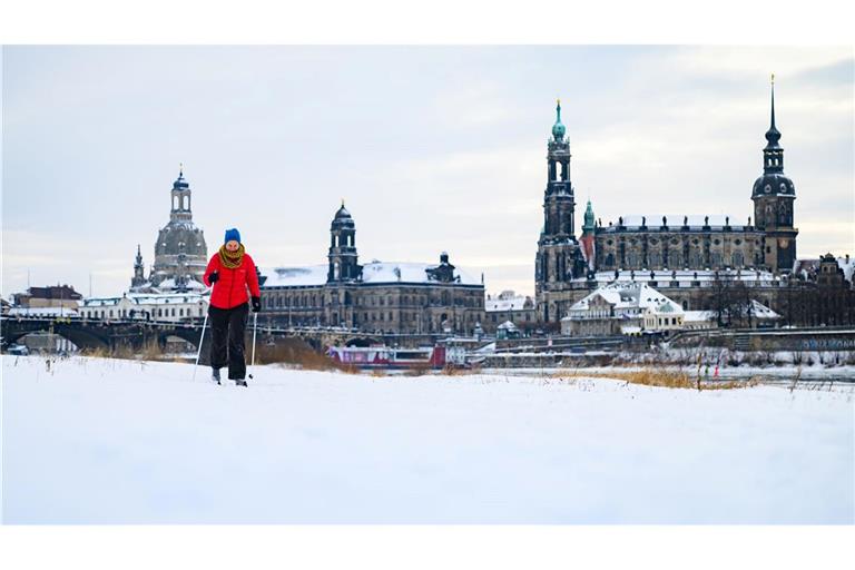 Eine Frau läuft am verschneiten Elbufer vor der historischen Altstadtkulisse in Dresden Ski