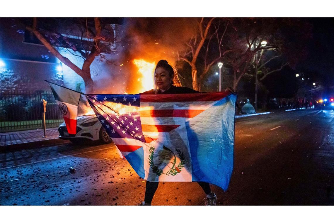 Bilder des Tages Eine Frau mit mehreren Flaggen geht an einem brennenden Auto vorbei, während sie gegen die Razzien der Trump-Regierung gegen Einwanderer in Los Angeles protestiert.