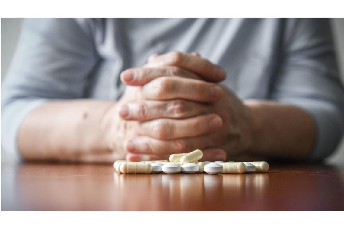 Warum die Zahl der Suizide in Deutschland weiter steigt Eine Frau sitzt mit gefalteten Händen an einem Tisch. Vor ihr liegt ein Haufen Tabletten (gestellte Szene).