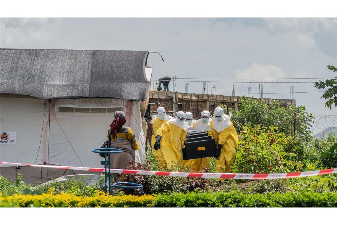 Eine Frau verfolgt, wie Mitarbeiter des Roten Kreuzes in Schutzanzügen den Sarg eines an Ebola Verstorbenen aus einem Gesundheitszentrum in Rwampara, Kongo, tragen.
