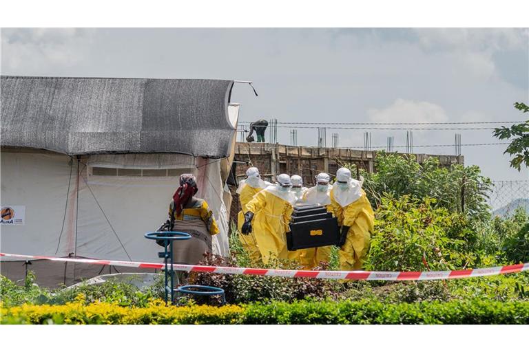 Eine Frau verfolgt, wie Mitarbeiter des Roten Kreuzes in Schutzanzügen den Sarg eines an Ebola Verstorbenen aus einem Gesundheitszentrum in Rwampara, Kongo, tragen.