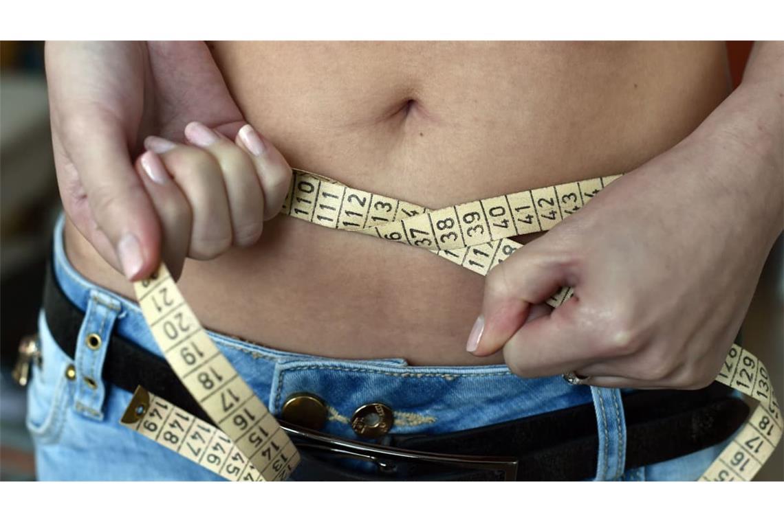 Eine junge Frau legt ein Maßband um ihren Bauch. Frauen sind öfter von Magersucht betroffen, aber auch Männer haben mit dem Problem zu kämpfen.