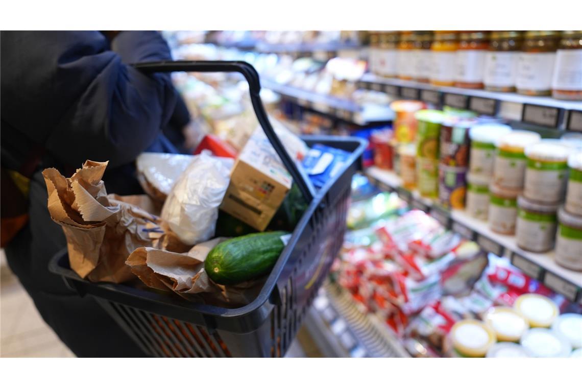Eine Kundin geht mit einem Einkaufskorb und ihrem Einkauf an den Regalen in einem Supermarkt vorbei.