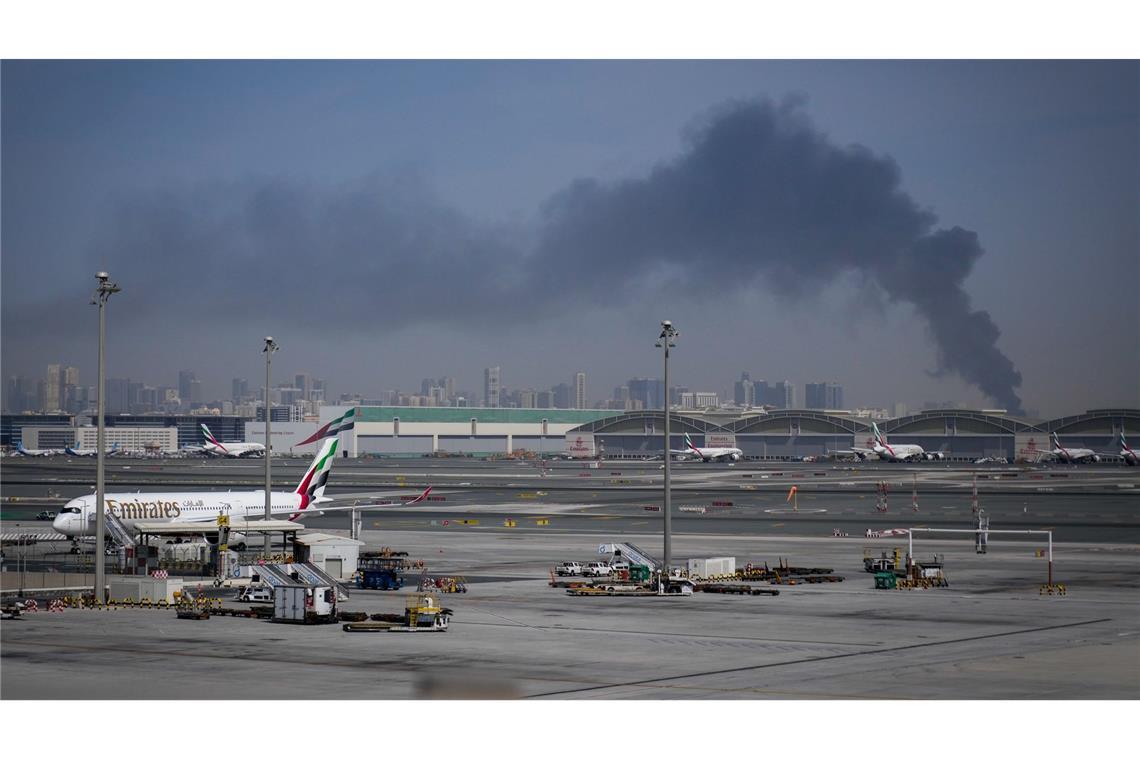 Eine Rauchwolke im Hintergrund, während Flugzeuge auf dem geschlossenen Dubai International Airport geparkt sind.