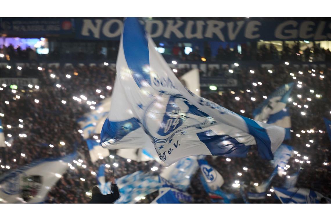 Eine Schalker Vereinsfahne weht vor dem Spiel gegen den 1. FC Magdeburg vor den Lichtern von Smartphones.