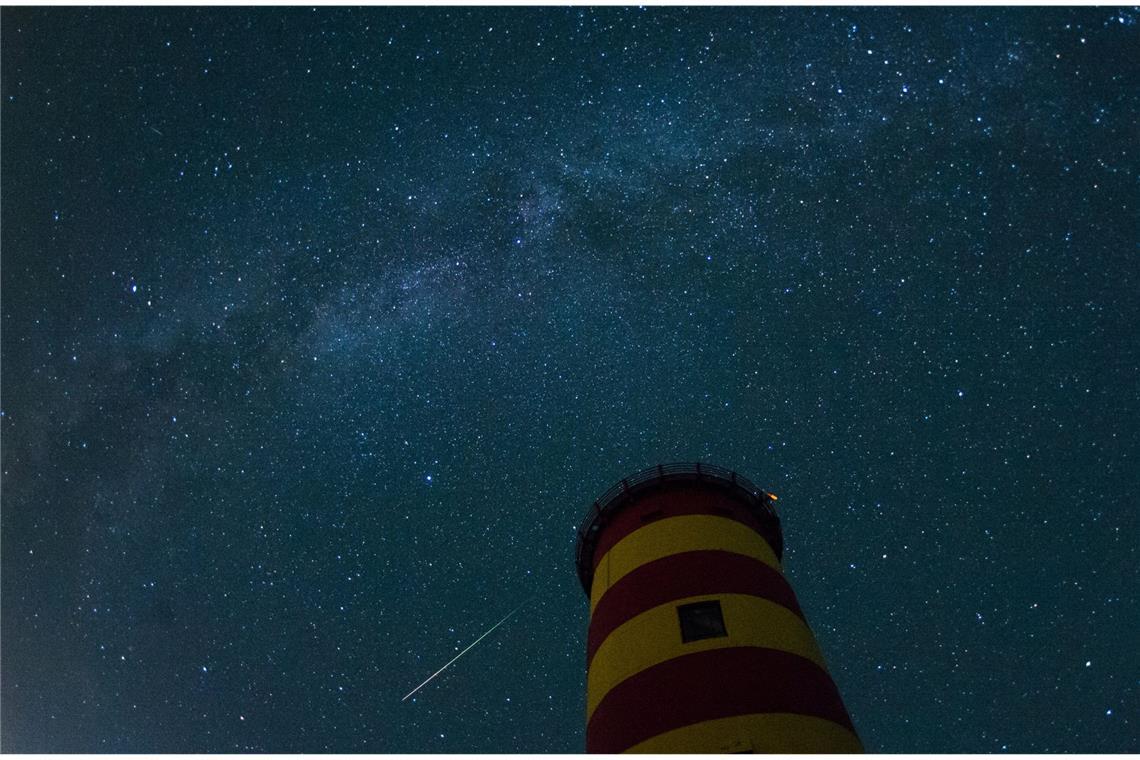Eine Sternschnuppe leuchtet im August 2015 über dem Pilsumer Leuchtturm in Niedersachsen am Nachthimmel.