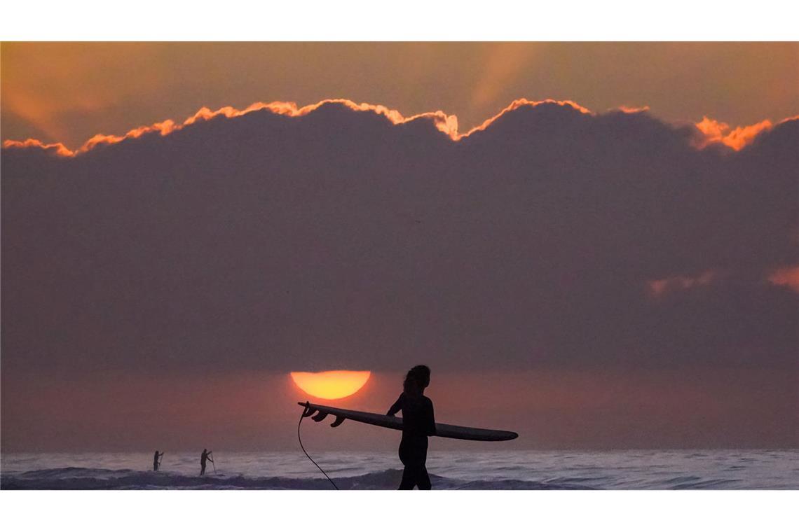 Eine Surferin trägt ihr Surfbrett in Richtung Meer.