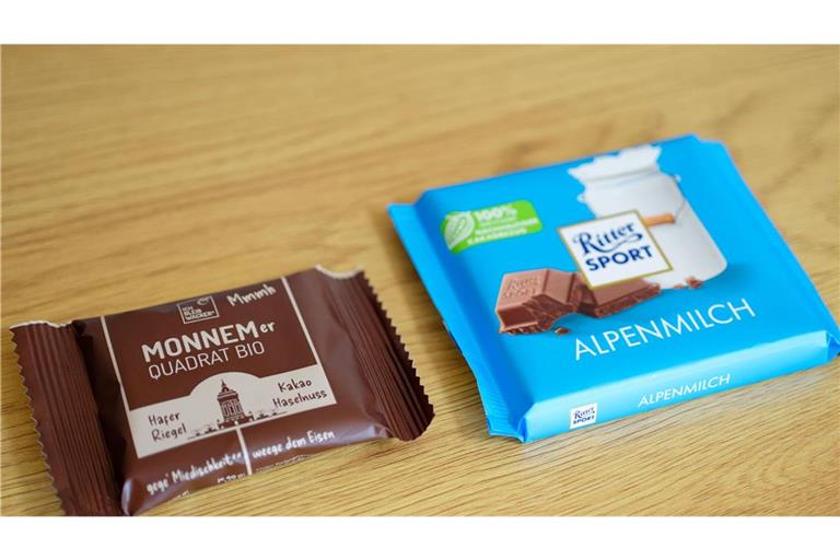 Eine Tafel mit Schokolade der Marke Ritter Sport (r) und ein Haferriegel der Firma Wacker mit der Aufschrift „Monnemer Quadrat Bio“ liegen nebeneinander auf einem Tisch.