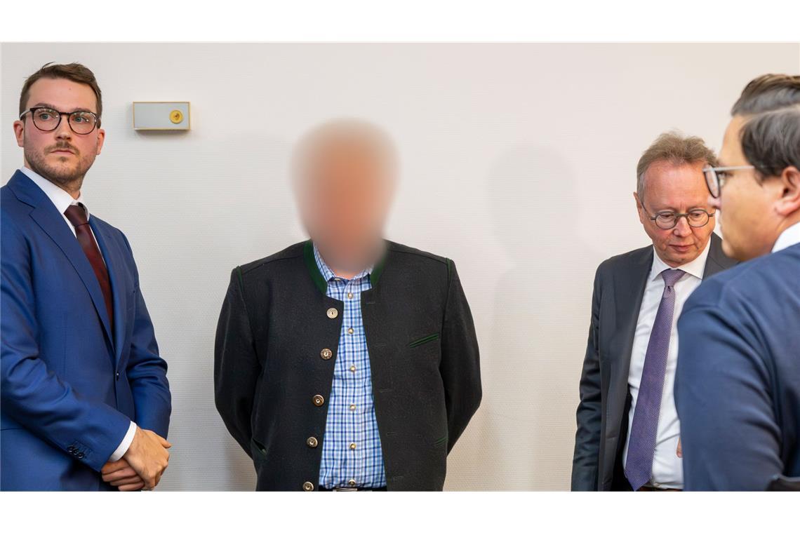 Einer der beiden beschuldigten Bahnmitarbeiter (M) steht vor Prozessbeginn zwischen Anwälten im Gerichtssaal des Landgerichts München.