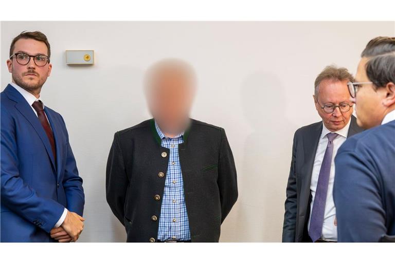 Einer der beiden beschuldigten Bahnmitarbeiter (M) steht vor Prozessbeginn zwischen Anwälten im Gerichtssaal des Landgerichts München.