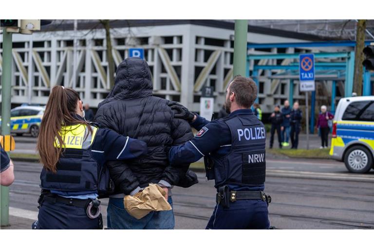 Einsatzkräfte der Polizei führen einen Mann in der Nähe von einem Tatort in Handschelllen ab.