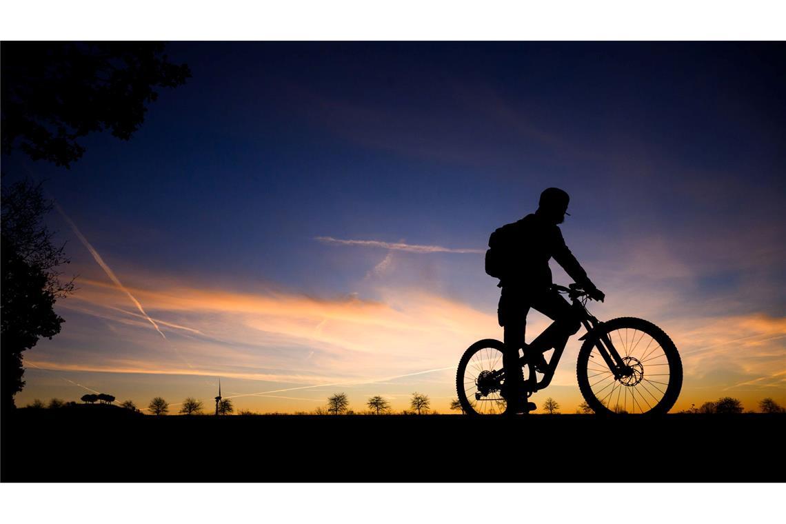 Fahrradfahrer im Morgengrauen: Silhouette vor Sonnenaufgangshimmel in Hannover.