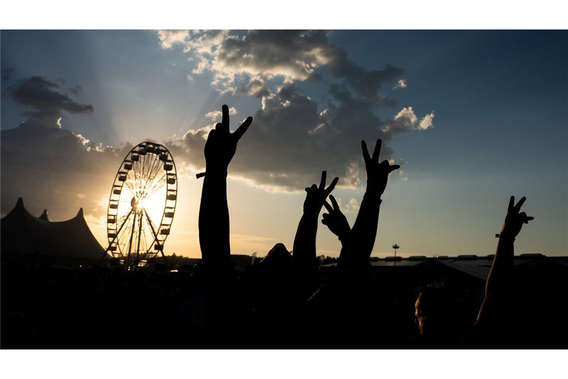 Festivalbesucher halten bei Sonnenuntergang ihre Hände auf dem Southside in die Höhe und sind dabei als Silhouette zu sehen.