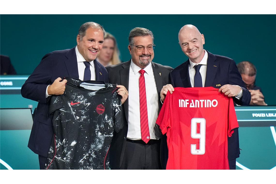FIFA-Präsident Gianni Infantino (r) präsentiert mit Vizepräsident Victor Montagliani (l) und Kanadas Fußballchef Peter Augruso ein kanadisches Nationaltrikot mit seinem Namen.
