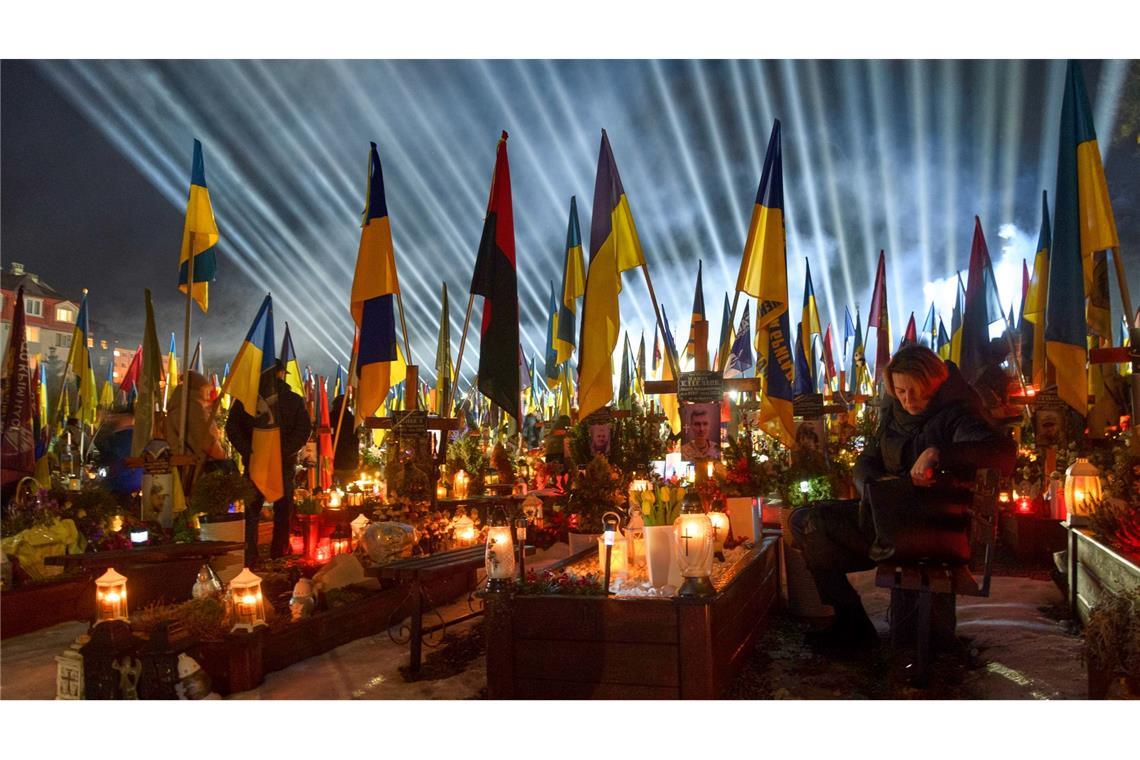 Flutlichter leuchten in Lwiw über den Gräbern der gefallener Soldaten, während Menschen am Vorabend des vierten Jahrestages der russischen Invasion Kerzen anzünden.
