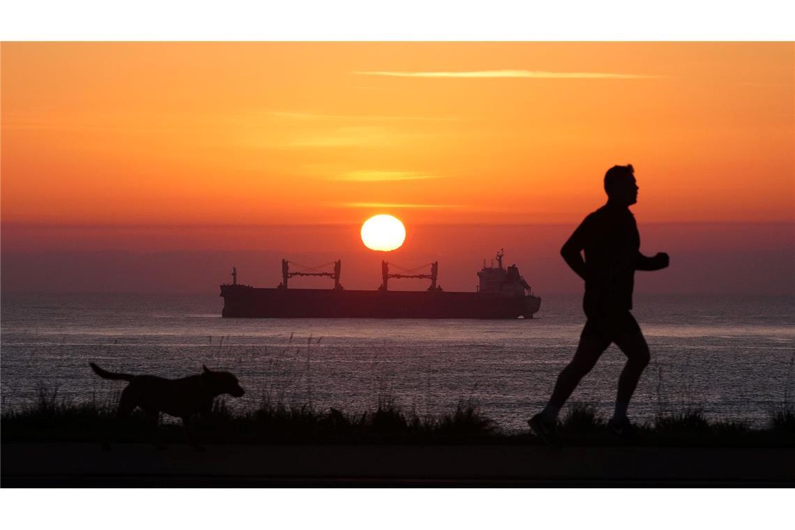 Früh unterwegs: Ein Mann joggt am Morgen an der Nordostküste von Großbritannien, während die Sonne am Horizont über einem Frachter aufgeht.