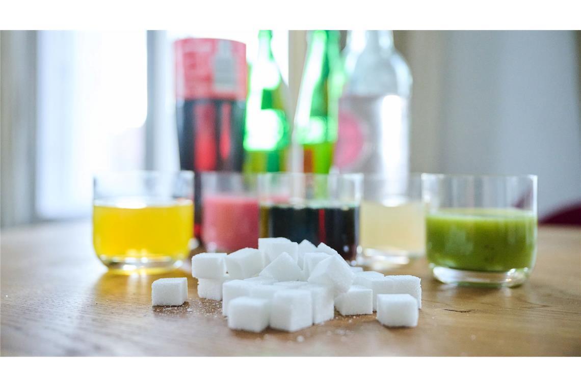Softdrinks erhöhen Risiko für Diabetes und Herzkrankheiten Fünf unterschiedliche Arten Softdrinks und die Flaschen dazu zusammen mit Zuckerwürfel auf einem Tisch