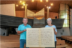 Helmut Stach und Monika Franke zeigen die übergroßen Notenblätter. Sie sind ein Erinnerungsstück an vergangene Zeiten des Chors aus dem Fundus des Ehrendirigenten und langjährigen Organisten Rudolf Marx. Foto: Stefan Bossow