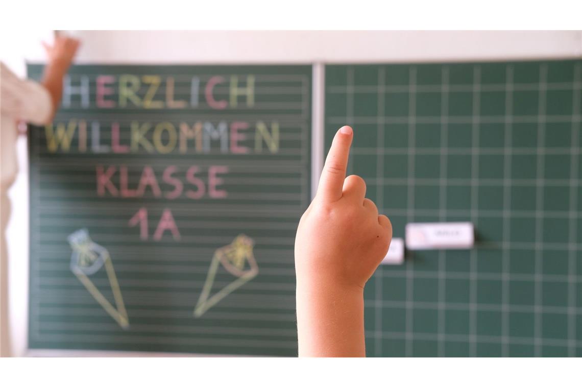 „Herzlich willkommen Klasse1 A“ steht an der Tafel eines Klassenzimmers, während sich ein Kind meldet. Am Samstag wird in Sachsen Einschulung gefeiert.