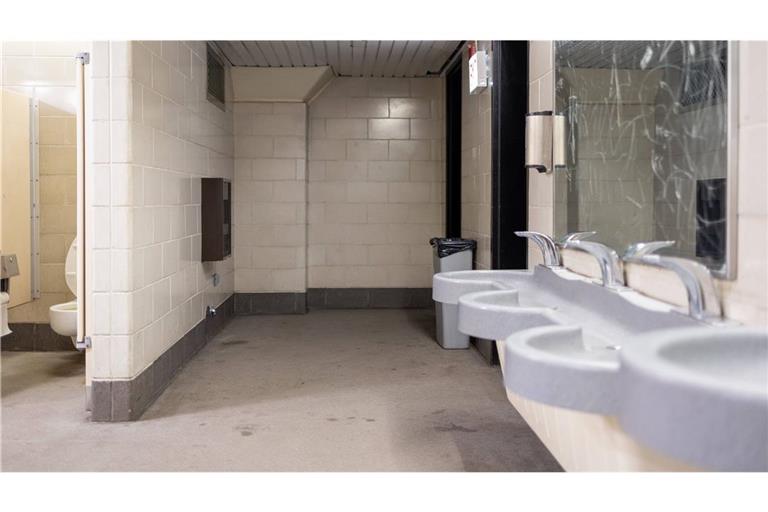 Innenansicht einer öffentlichen Toilettenanlage mit Waschbecken, Urinalen und einzelnen WC-Kabinen. Der Raum ist funktional gestaltet mit Fliesenwänden, Trennwänden und standardisierten Sanitäranlagen. Mulmig ist es einem trotzdem, wenn man an einem solchen Ort muss.