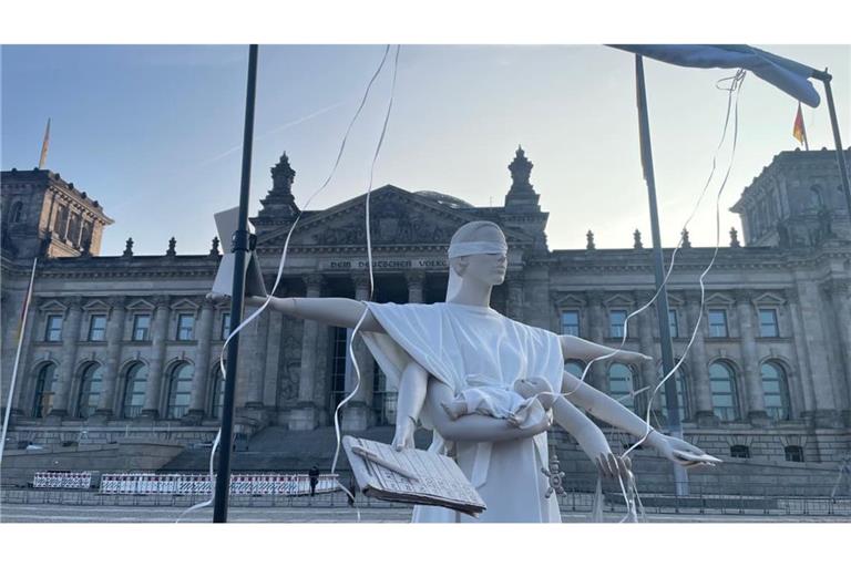„Justitia ohne Mutterschutz“&nbsp;– die&nbsp;Symbolfigur für Gerechtigkeit steht mit sechs Armen, Babybauch, Kind und vielen ungesehenen Aufgaben vor dem Reichstagsgebäude.