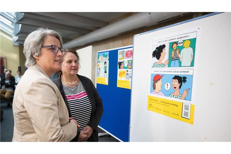 Kerstin Claus (links) und Theresa Schopper schauen ein Plakat gegen sexualisierte Gewalt an.