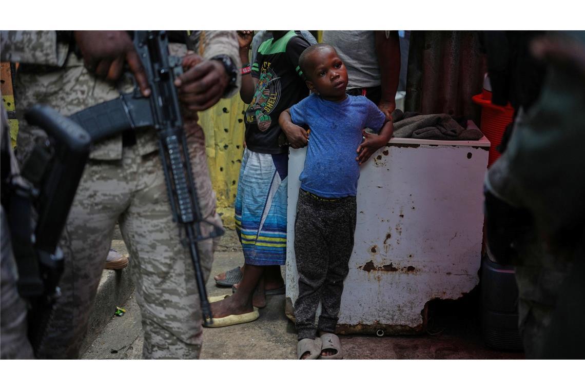 Kind neben bewaffnetem Polizisten in Unterkunft für Vertriebene in Port-au-Prince