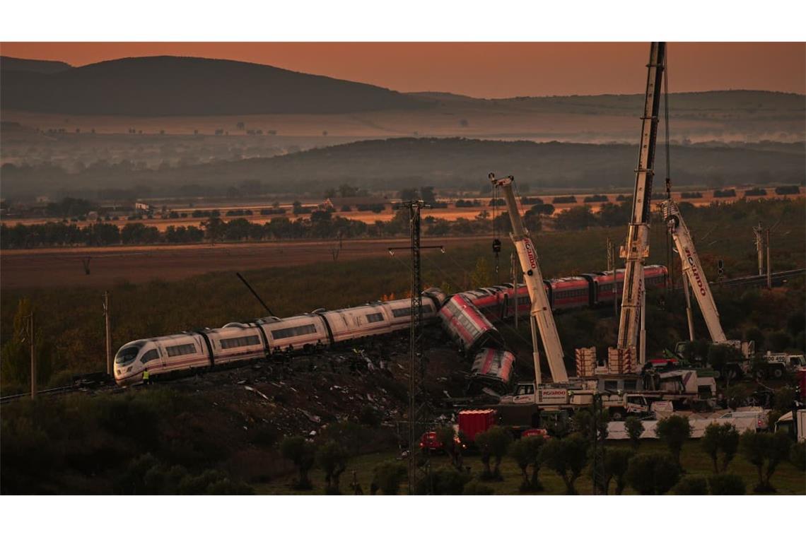 Kräne heben zerstörte Zugwaggons an, während Rettungskräfte nach der Kollision zweier Züge nach Opfern suchen.