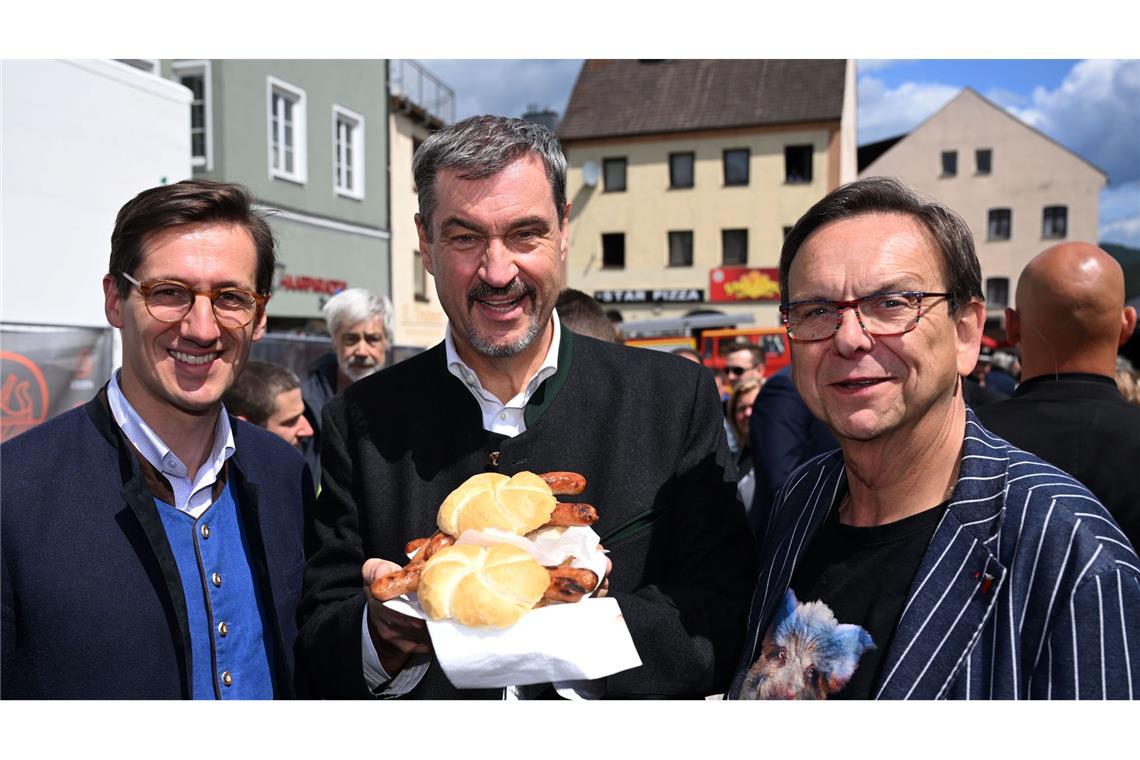 Schweine-Wettgrillen mit Söder und Peta-Protest Markus Söder (M.) hält Bratwurst-Semmeln in die Kamera.