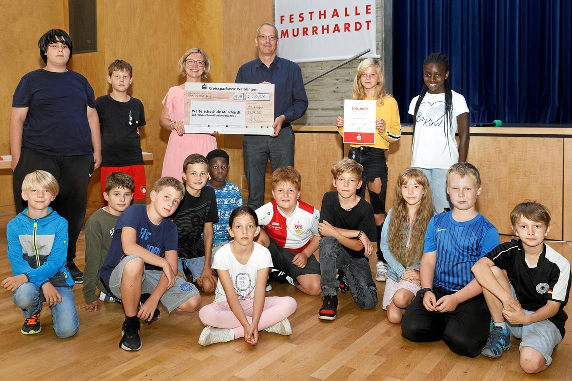 Motivierte Schüler, motiviertes Lehrerduo Martin Keller von der Kreissparkasse überreicht Sarah Wilken einen symbolischen Scheck. Die Dritt- und Viertklässler haben 2021 beim Sportabzeichenwettbewerb gepunktet und 2000 Euro für die Walterichschule geholt. Fotos: Jörg Fiedler