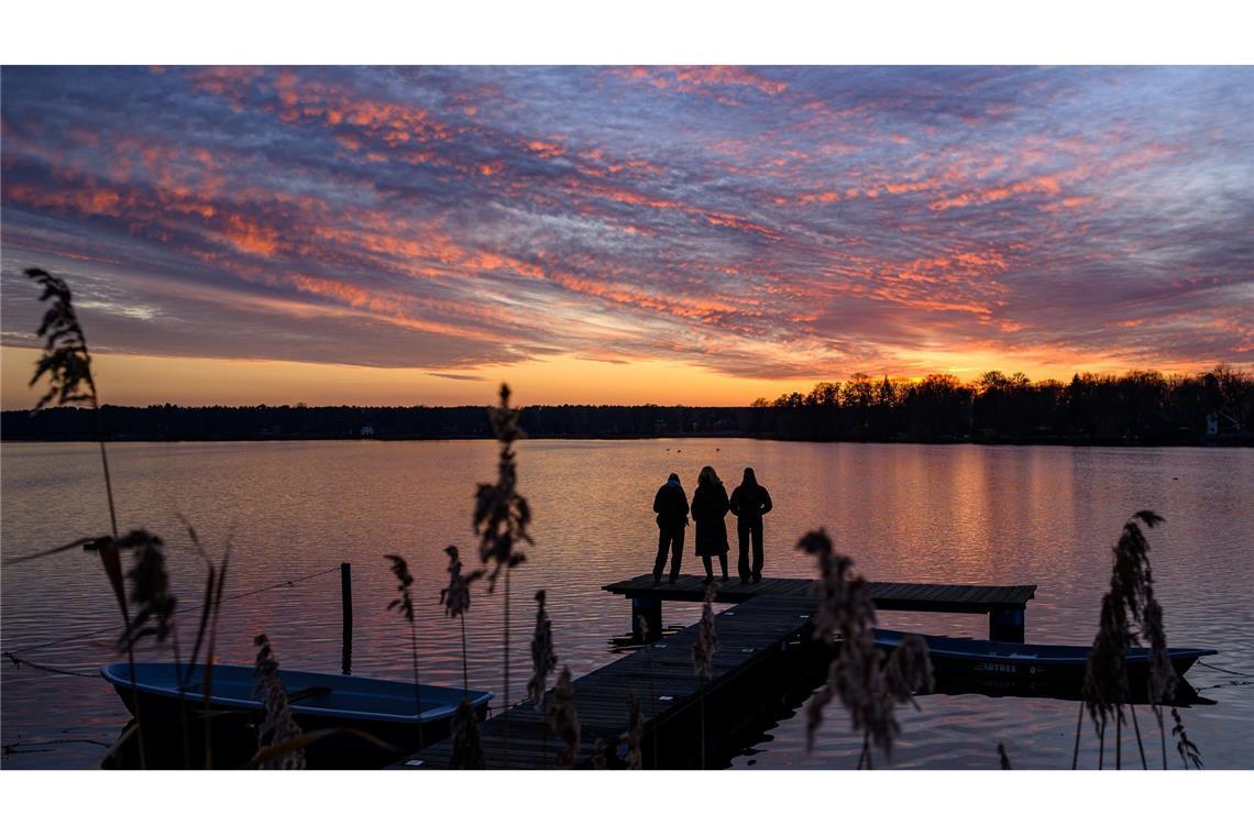 Bilder des Tages Menschen auf einem Steg beobachten, wie die Wolken zum Sonnenuntergang über dem Großen Müllroser See im östlichen Brandenburg farbenprächtig leuchten.