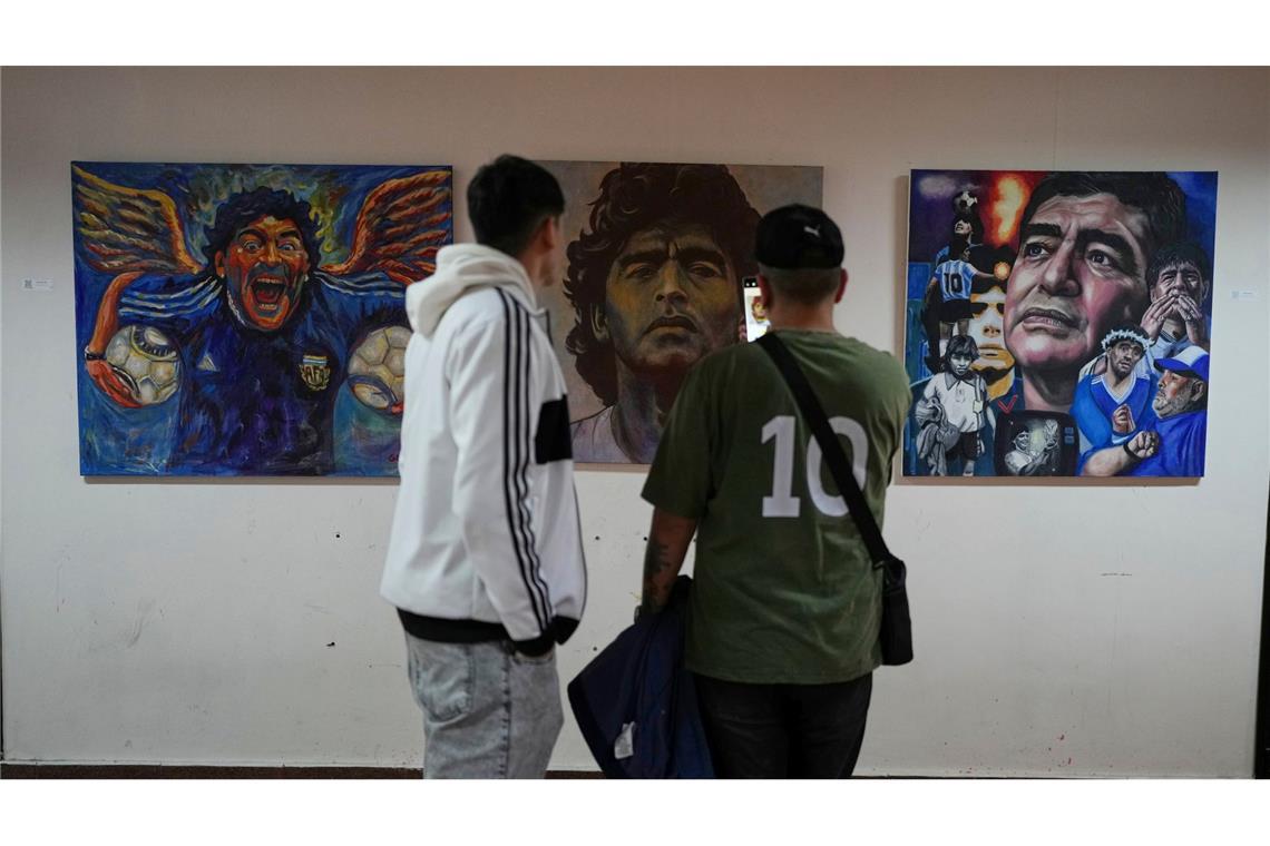 Menschen betrachten eine Kunstausstellung mit Bildern des verstorbenen Fußballstars Maradona.