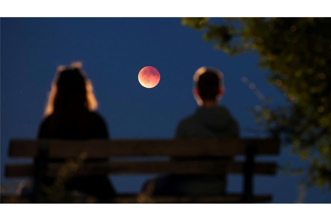 Bilder des Tages Menschen betrachten von einer Parkbank aus die auch als Blutmond bezeichnete totale Mondfinsternis in Leipzig.