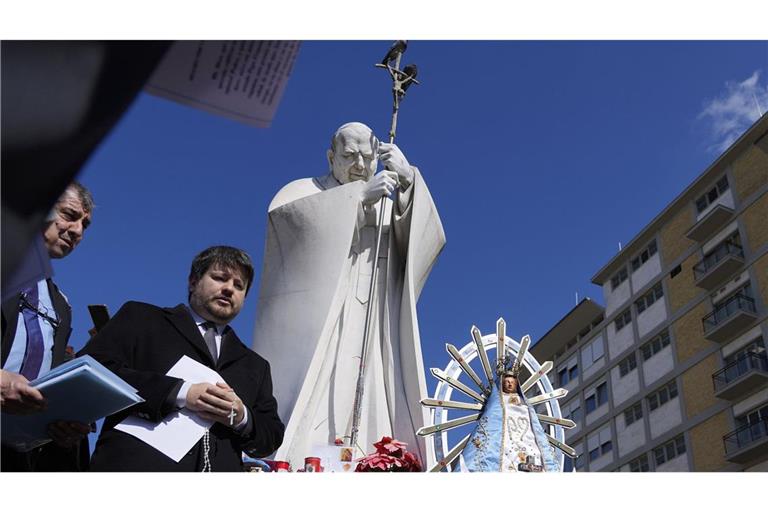 Menschen sitzen bei der Statue von Papst Johannes Paul II. auf dem Gelände der Poliklinik Agostino Gemelli, wo Papst Franziskus seit Mitte Februar behandelt wird.