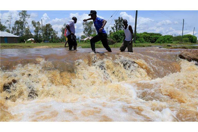 Menschen überqueren einen überfluteten Straßenabschnitt nach schweren Regenfällen in Ahero, Kenia.