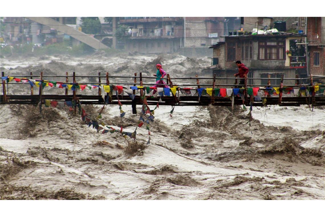 Bilder des Tages Menschen wagen im nordindischen Bundesstaat Himachal Pradesh trotz schwerer Überschwemmungen den Weg über eine Brücke, um den Fluss Beas zu überqueren.