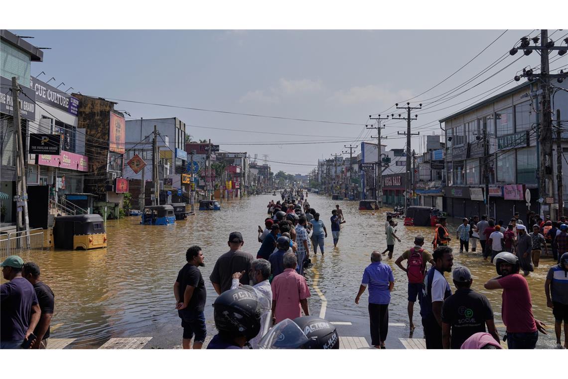 Menschen waten durch ein überschwemmtes Gebiet in Sri Lanka.