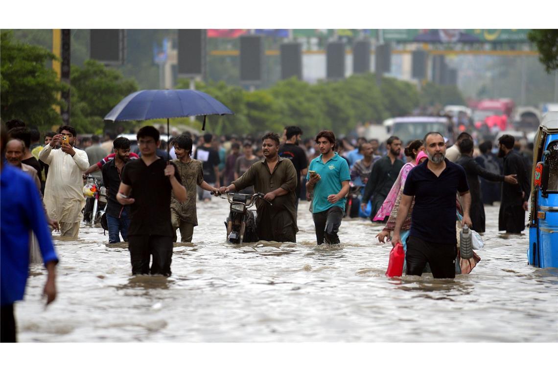Menschen waten durch eine überflutete Straße nach starkem Monsunregen in Pakistan.